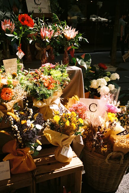 A vibrant display of fresh floral arrangements and bouquets at a flower shop, featuring a variety of flowers including pink lilies with large petals, bright red and orange gerbera daisies, delicate wh
